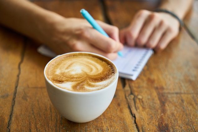 Apartments for rent in Spring TX A person diligently jotting down notes in a notebook, situated alongside a steaming cup of coffee.