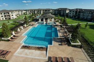 Apartments in Tomball, TX - Elevated View of Pool, Patio with Lounge Chairs, Clubhouse and Apartment Buildings
